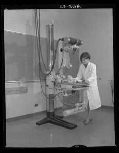 B&W archival image of a woman in a labcoat at a microscope